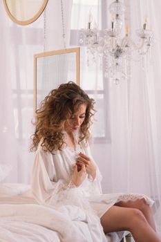 Young woman in a white lace robe sitting indoors under a chandelier.