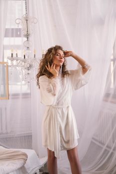 A young woman poses with closed eyes in an elegant white robe under a chandelier.