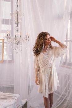 A bride standing indoors in a white robe, exuding elegance and grace.