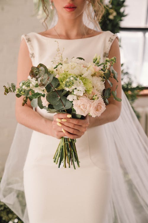 Woman in Bridal Gown Holding Bouquet of Flowers