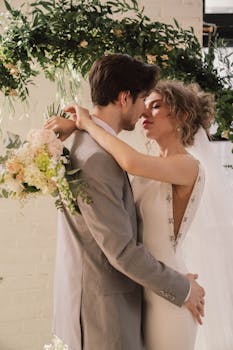 Romantic wedding couple embracing under floral arch inside a venue.