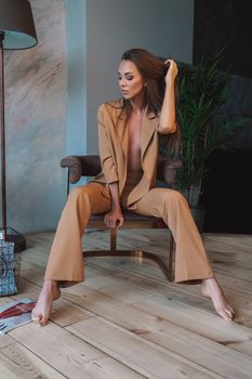 Woman in a brown suit sitting barefoot indoors, exuding sophistication and style.