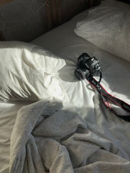 DSLR camera resting on unmade bed in soft morning light, capturing a cozy, candid atmosphere.