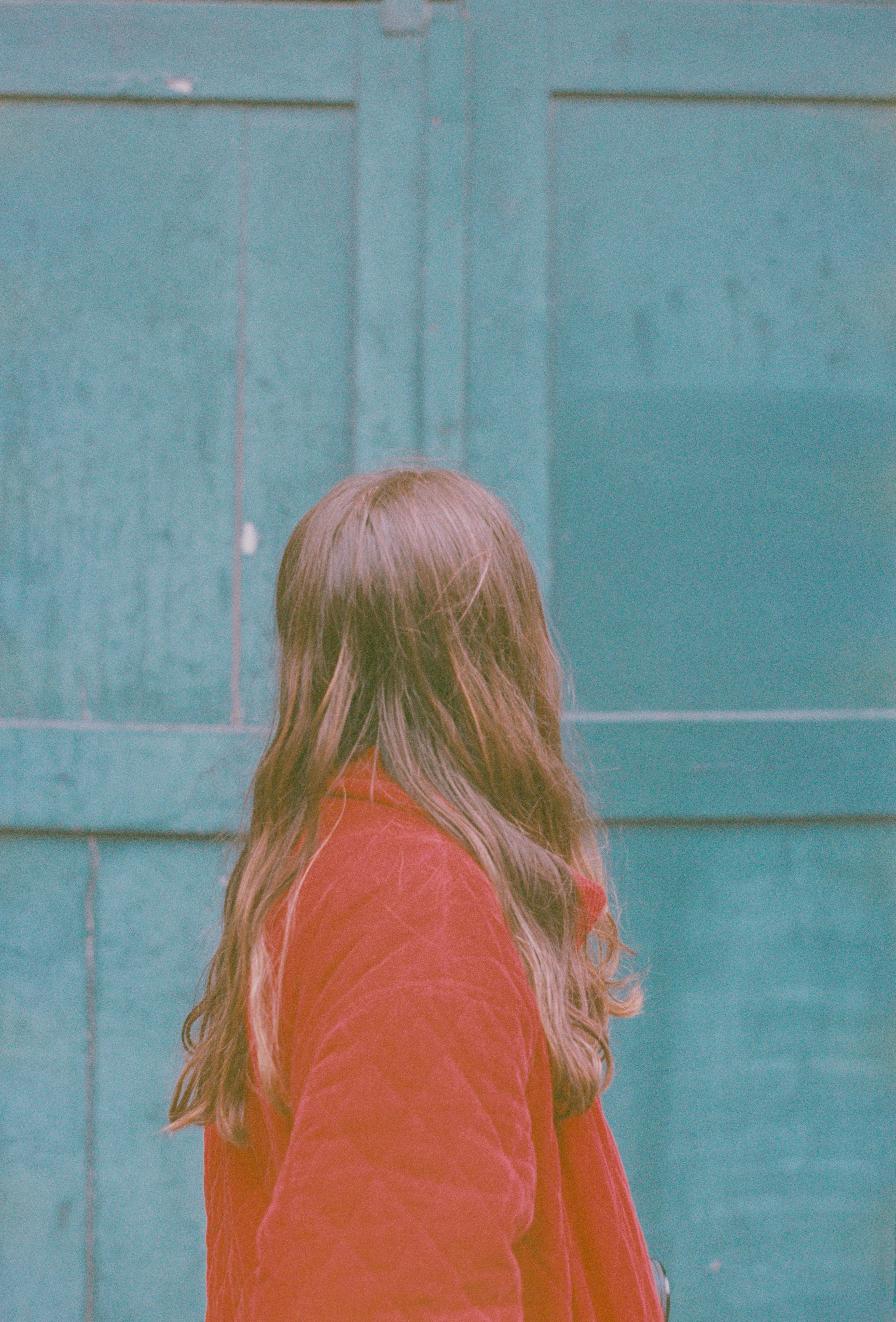 Back view of a woman in a red coat facing a rustic blue wall in Bruges, Belgium.