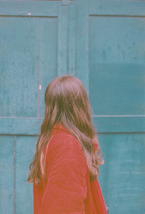 Free Back view of a woman in a red coat facing a rustic blue wall in Bruges, Belgium. Stock Photo