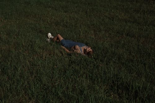 Free A woman in casual overalls relaxes on a grassy field under the open sky, enjoying nature. Stock Photo