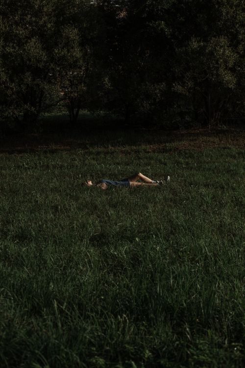 Free A person lying down in a lush green field surrounded by trees, enjoying nature. Stock Photo