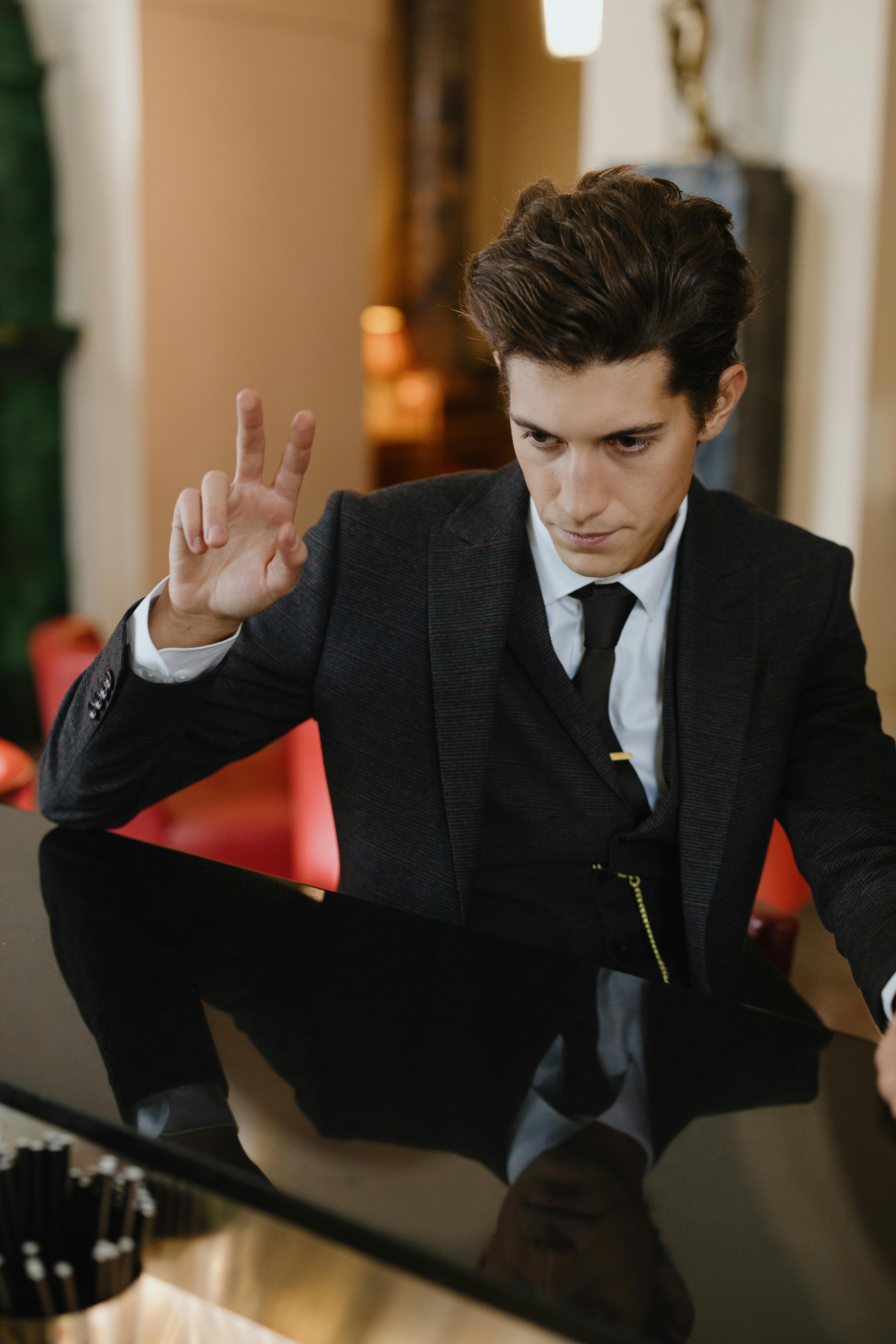 A young man in a formal suit gestures with fingers at a bar counter indoors.