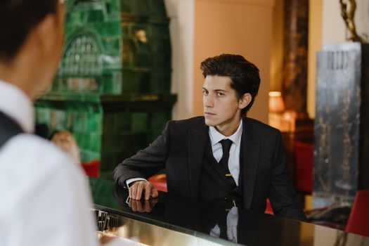 Sophisticated man in a suit sitting at a vintage bar counter indoors, exuding elegance and style.