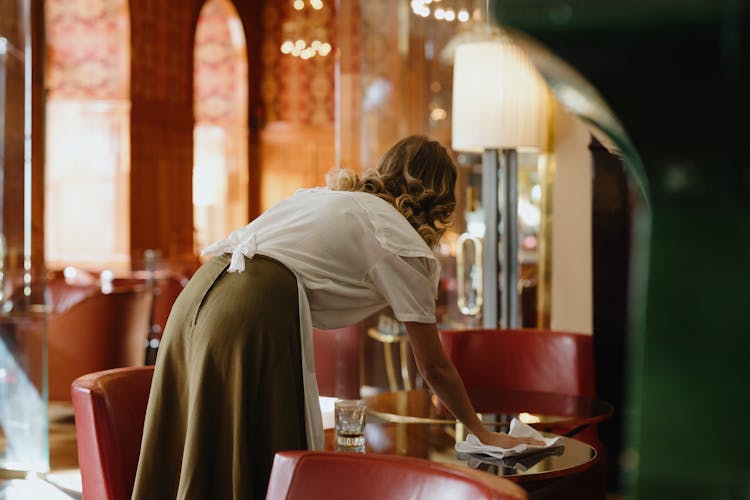 A Woman With Apron Wiping The Table