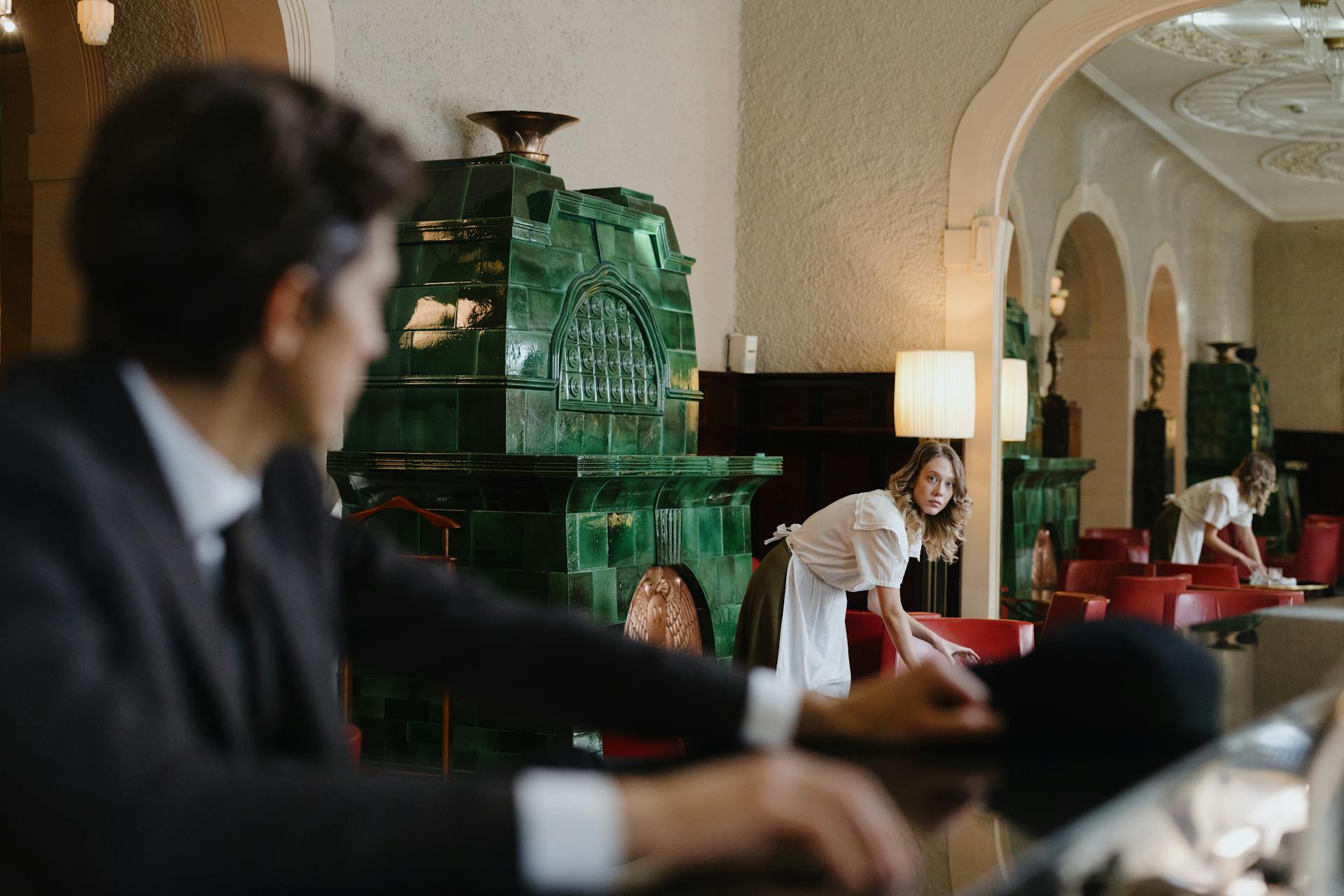 A sophisticated restaurant interior showing a waitress arranging tables while a host observes, highlighting elegance and service.