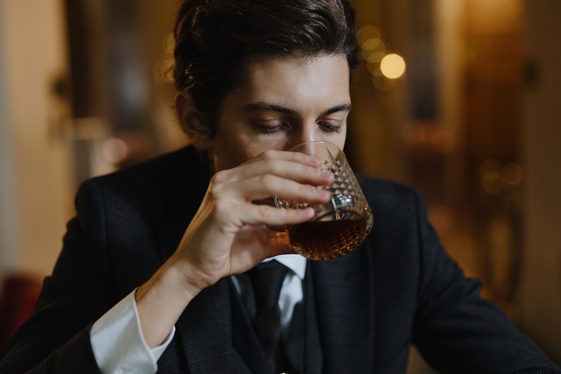 A close-up of a hand pouring a neat bourbon into a rocks glass on a bar