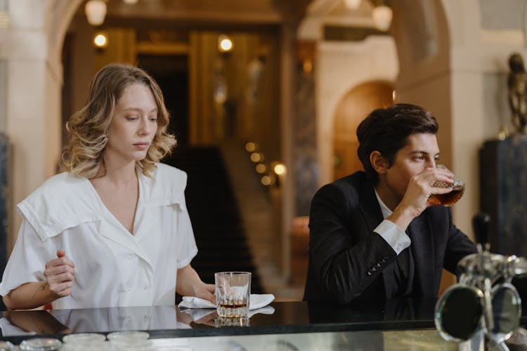 A Woman In White Top Standing Beside A Man Drinking Whiskey