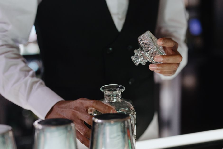 A bartender skillfully handles a crystal glass decanter at a stylish bar setting. A bartender skillfully handles a crystal glass decanter at a stylish bar setting.