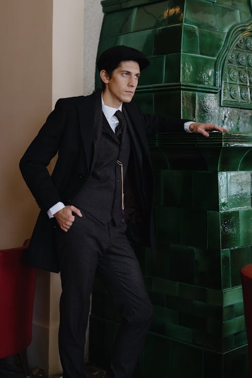 A Man in Black Suit Standing Beside a Green Wall