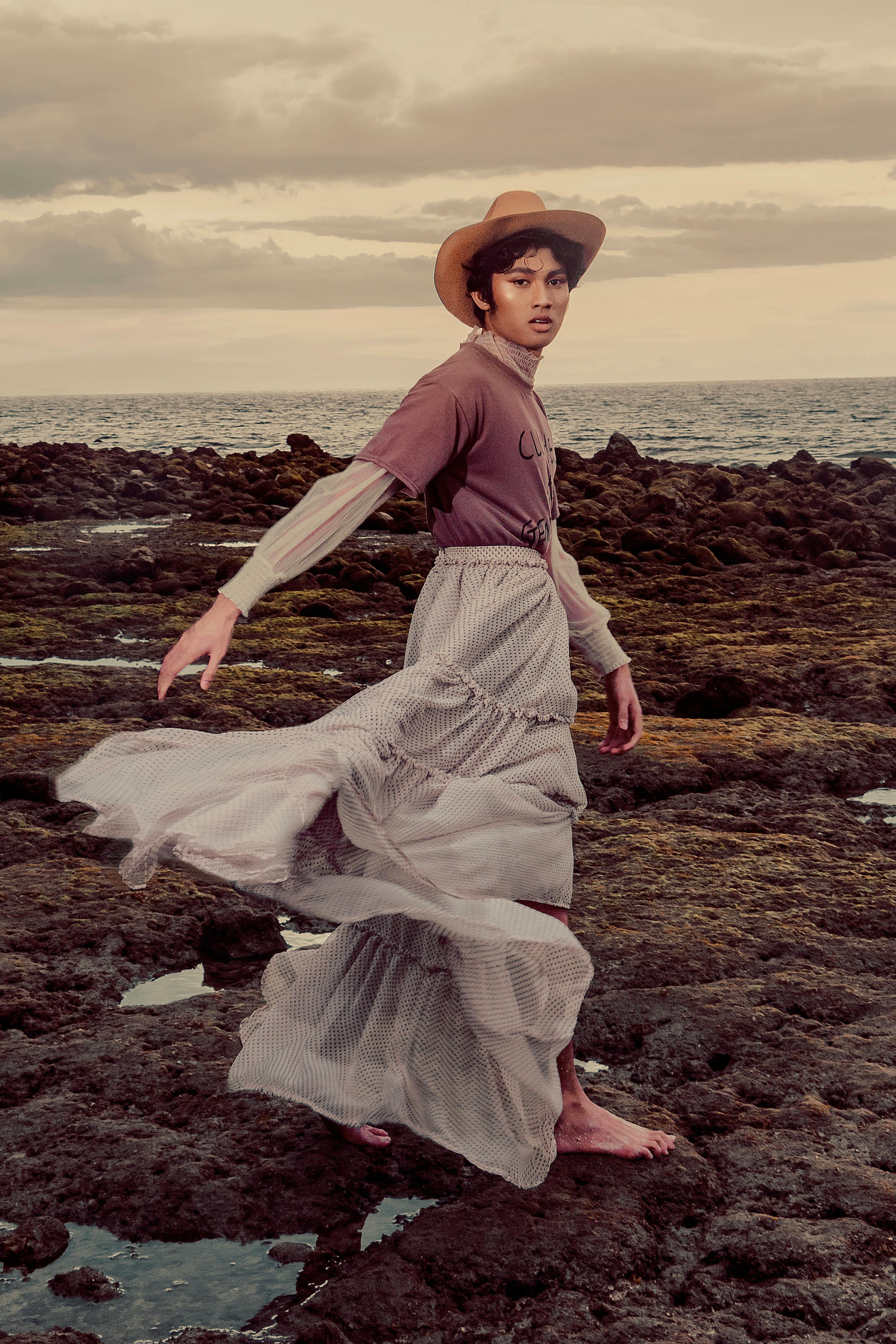 Elegant model in chic attire posing on rocky coast at sunset, showcasing motion and style.