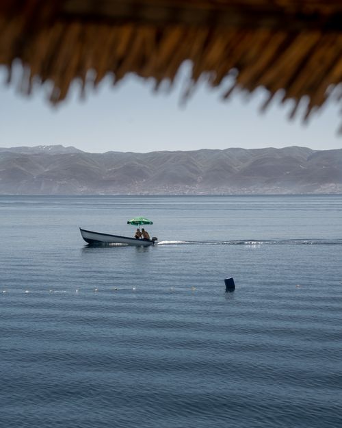Free Man on a boat with green umbrella on sunny lake, mountains in view. Stock Photo