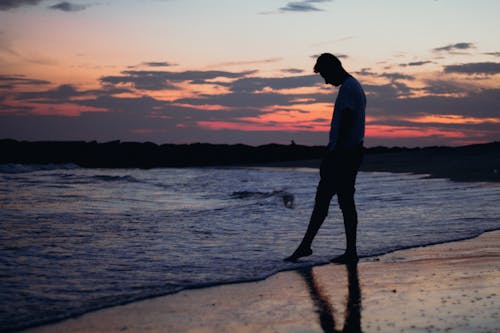 Free Silhouette of a Person Standing on the Beach during Sunset Stock Photo