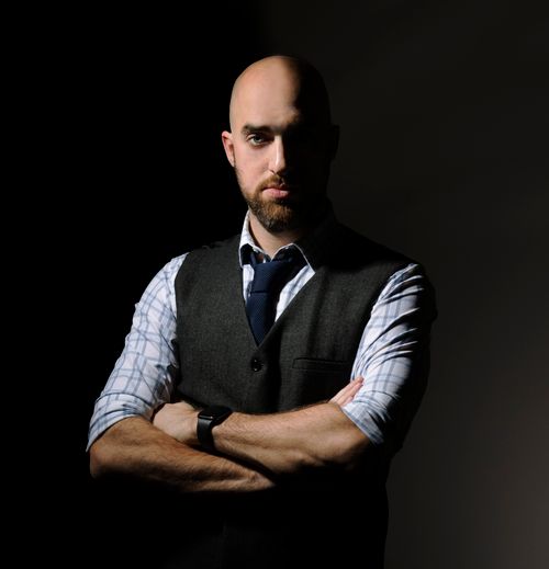 Free Dark and moody portrait of a confident bald man with beard, wearing a vest and tie. Stock Photo