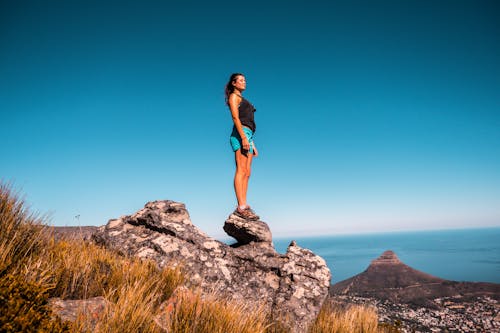 Woman in Black Top and Blue Shorts on Stone Under Blue Sky