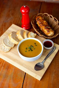 Delicious bowl of soup served with fresh bread slices on a wooden board.