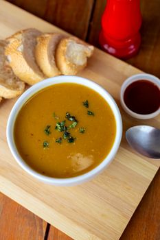 Warm pumpkin soup garnished with herbs, accompanied by sliced bread on a wooden tray.
