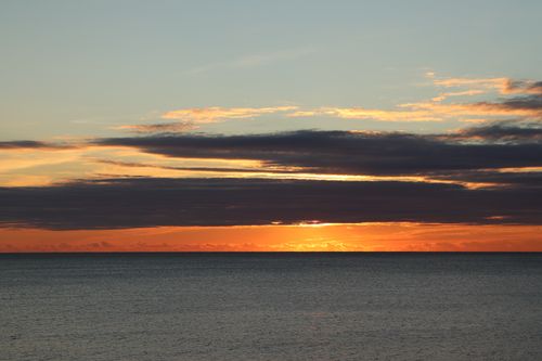 Free A breathtaking view of the sun setting over the calm ocean, showcasing vibrant skies and serene waters. Stock Photo