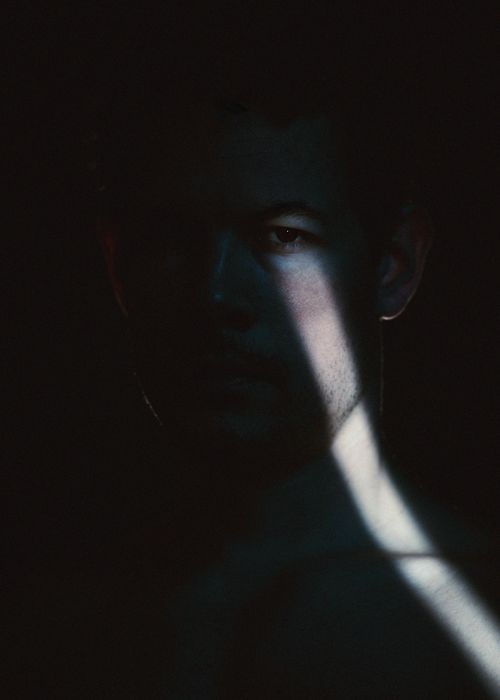Free Dramatic low-key portrait of a man with a streak of light revealing part of his face. Artistic composition. Stock Photo