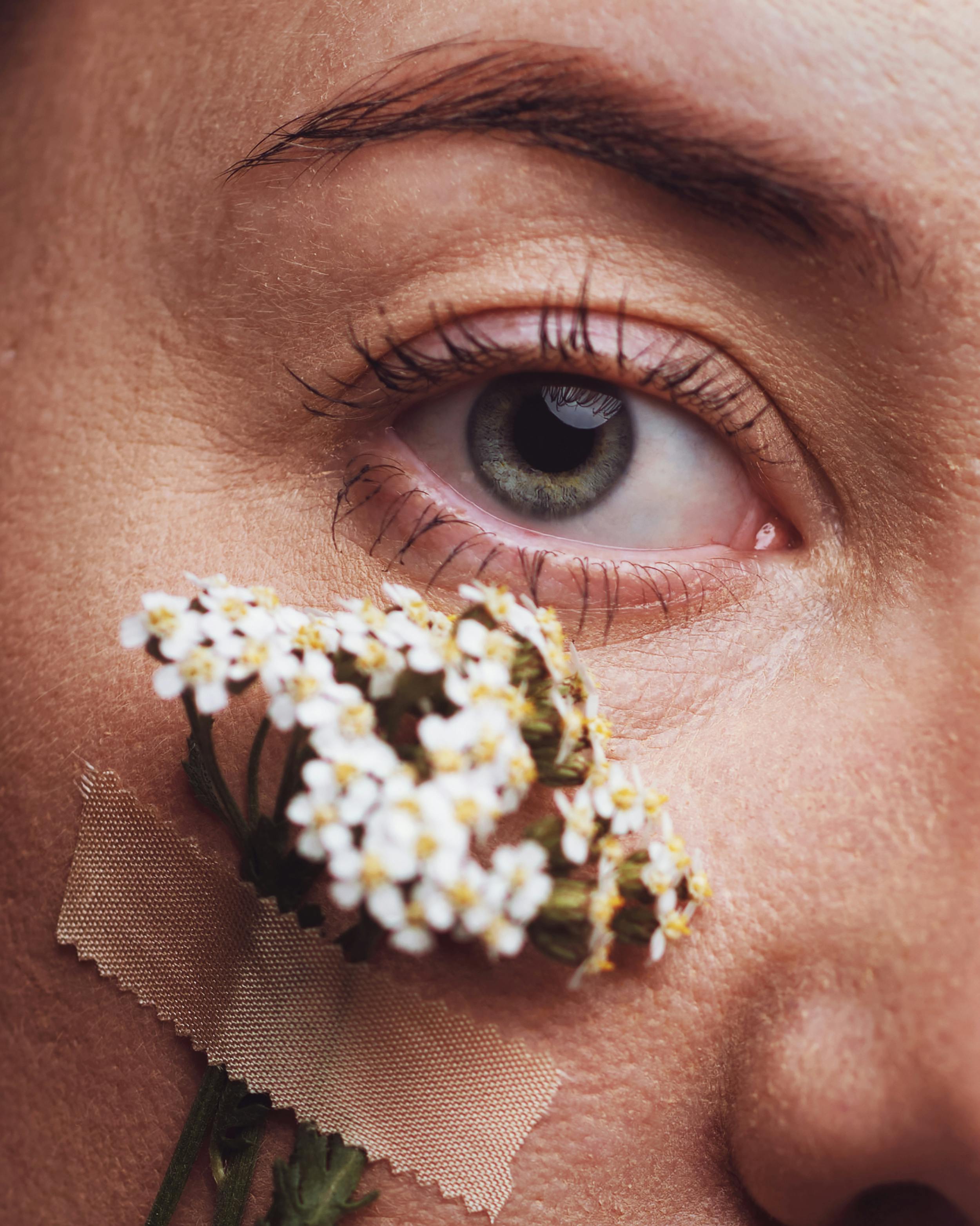 Artistic close-up shot of an eye with a small flower and band-aid on the cheek, conveying creativity.