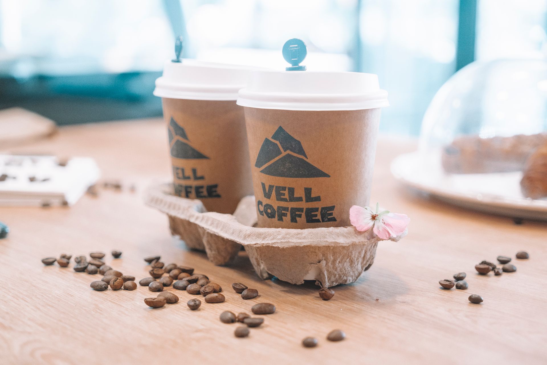 Stylish disposable coffee cups with flowers and beans on a wooden table.