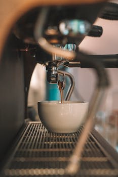 A warm shot of freshly brewed espresso filling a white ceramic cup in a coffee machine.