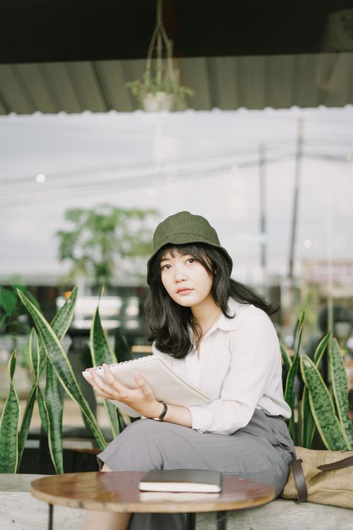 Free Woman in casual attire holding a notebook, sitting outdoors. Stock Photo