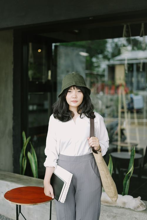 Free Young Asian woman in casual outfit posing outdoors, holding notebooks and carrying a bag. Stock Photo