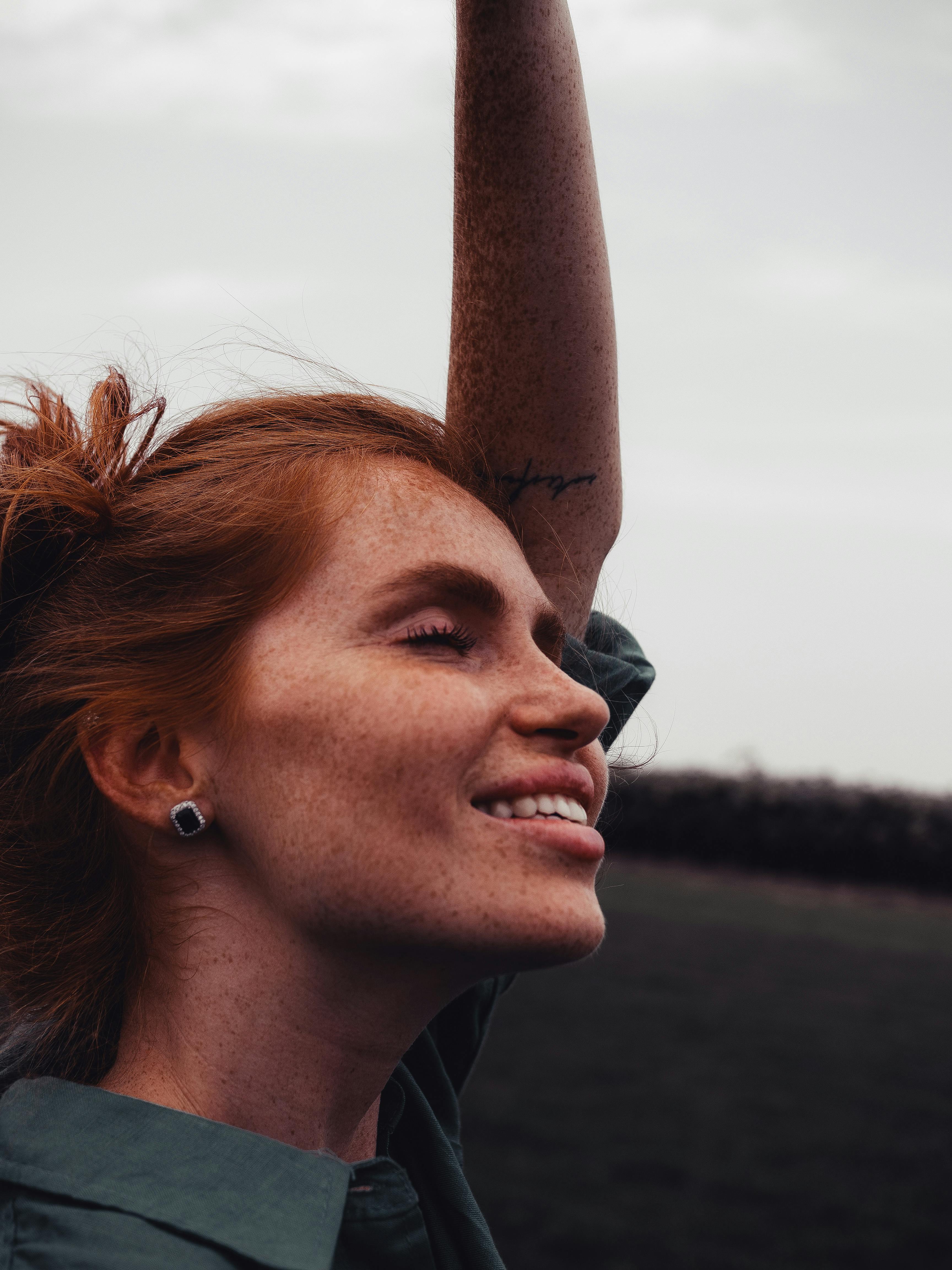 Close-up of a smiling woman with freckles enjoying the outdoors, eyes closed in serenity.