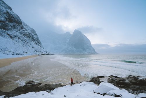 Free A solitary figure stands on a snowy beach in Flakstad, Norway, surrounded by winter landscapes. Stock Photo