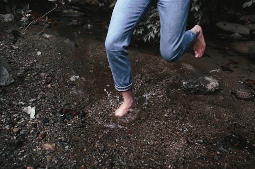 Person in Denim Pants Hopping Barefoot on Shallow Water