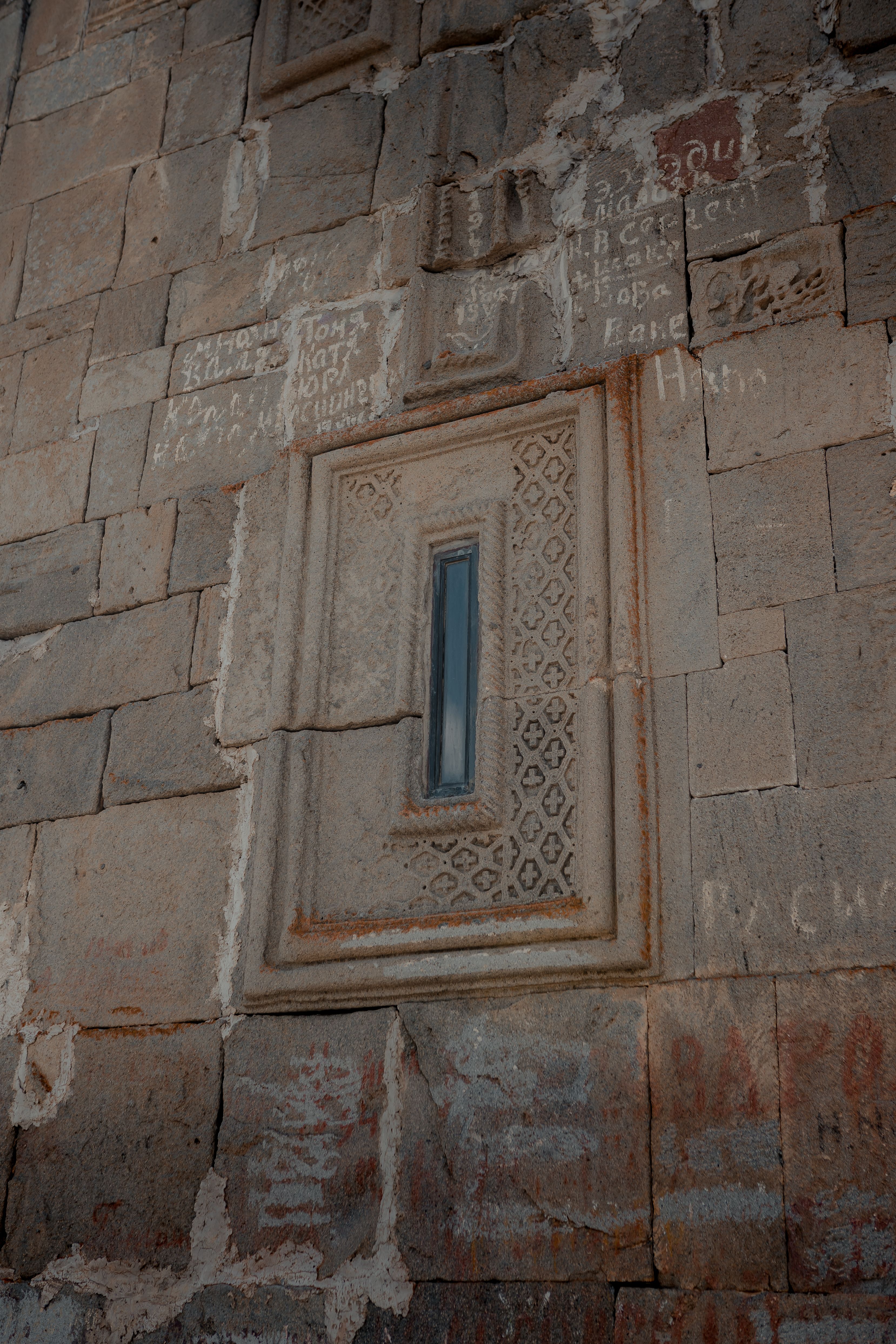 Detailed view of a historic stone wall featuring an ornate window and ancient inscriptions.