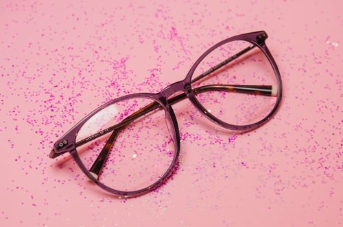 Free Stylish eyeglasses resting on a sparkling pink surface with scattered glitter elements. Stock Photo