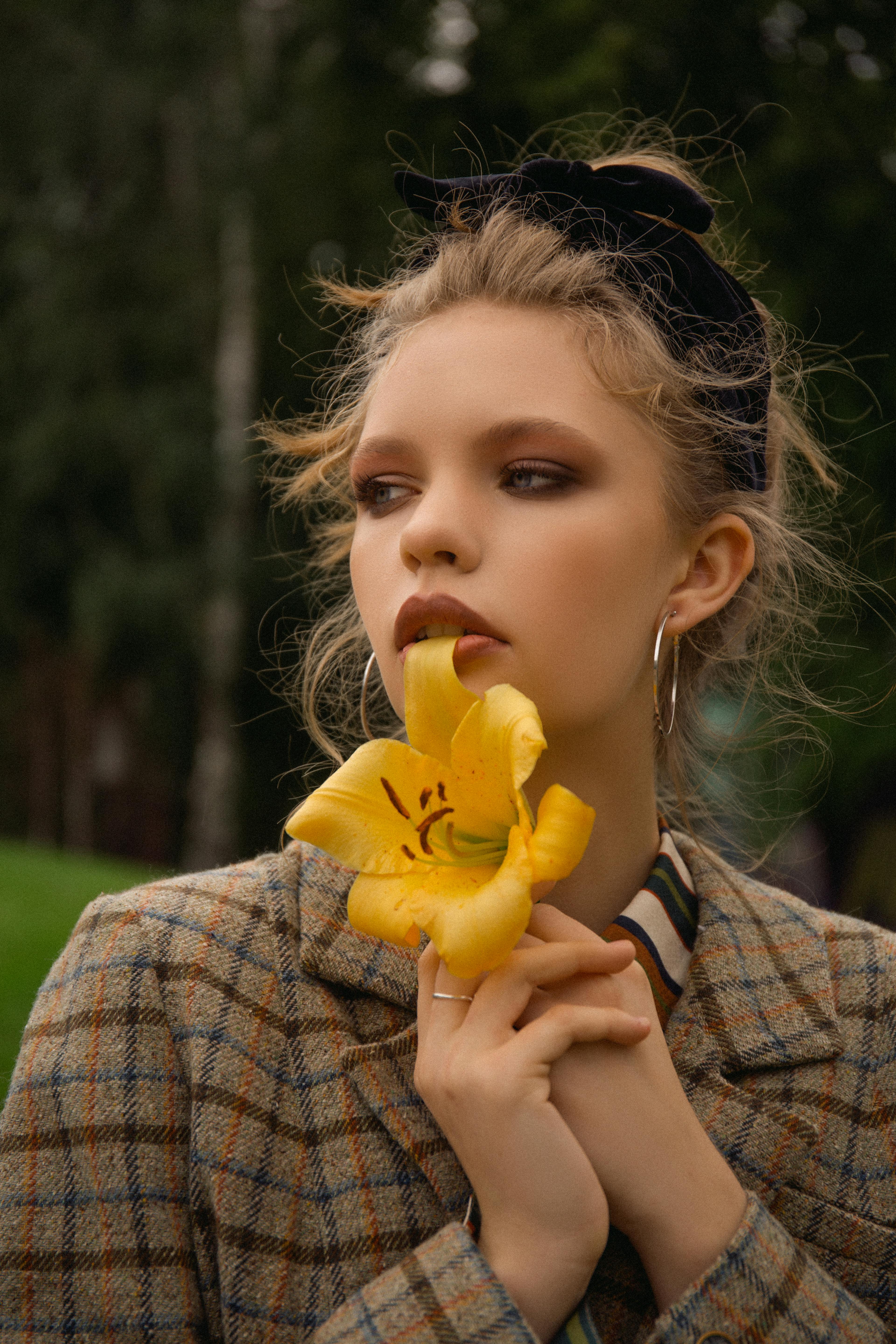 Beautiful woman holding a yellow lily with a blurred background. Outdoors portrait.