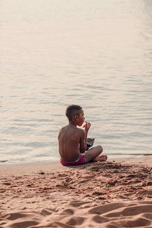 Topless Boy Sitting on Sand at the Beach