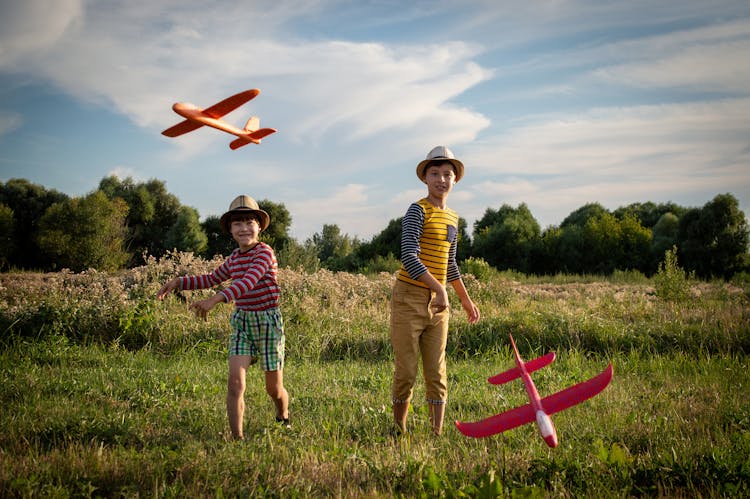 Boys Playing With Toy Planes In A Grass Field