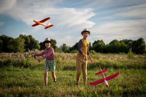 Free Two boys enjoying a sunny day in the countryside, playing with toy planes in an open field. Stock Photo