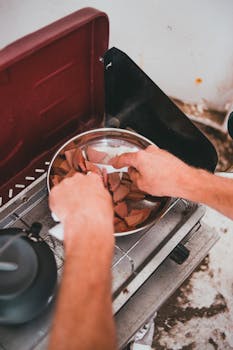 Close-up of hands arranging food on a portable grill during an outdoor camping adventure.