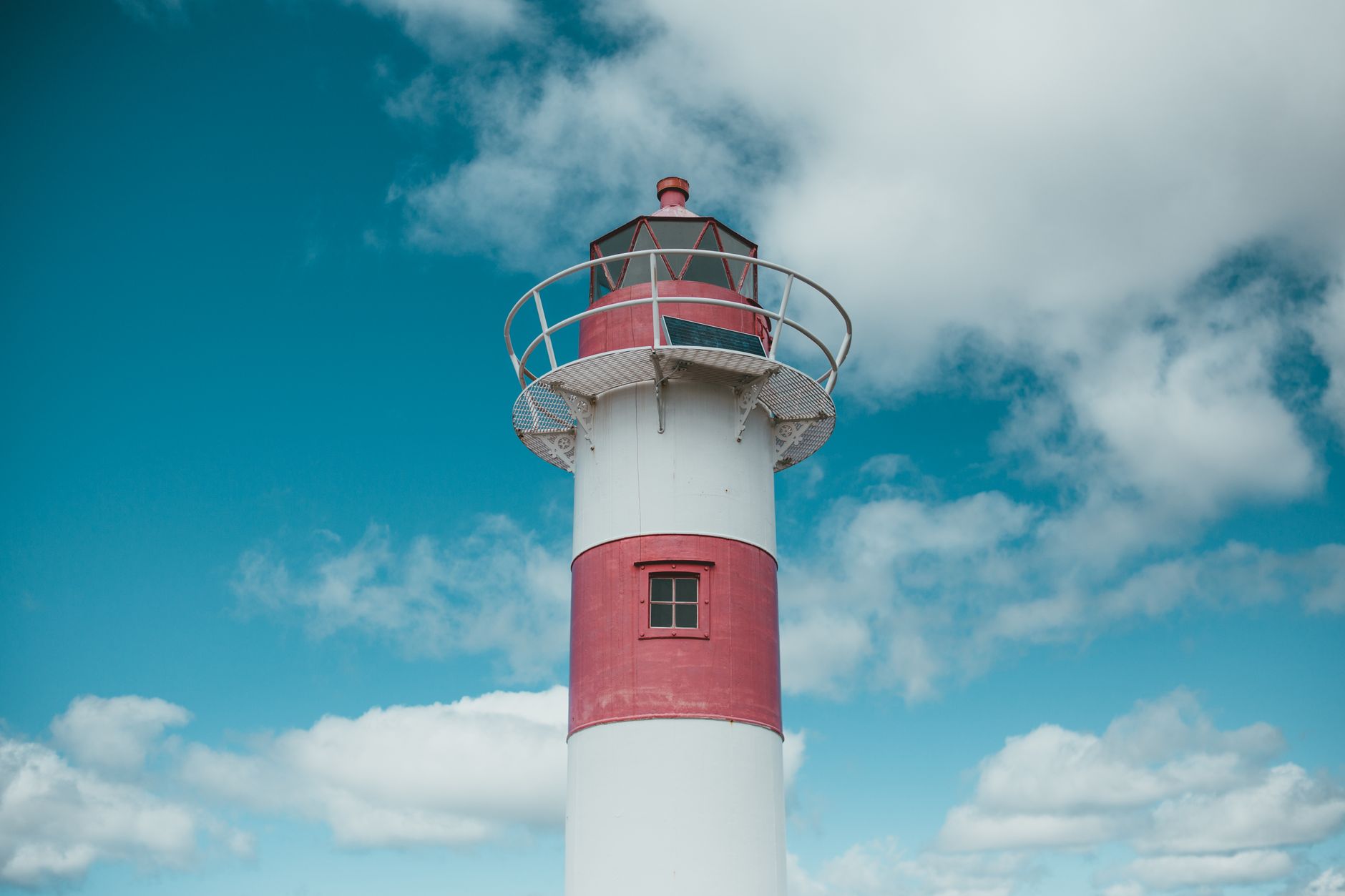 A vibrant red and white lighthouse stands tall against a backdrop of a clear blue sky and scattered clouds.
