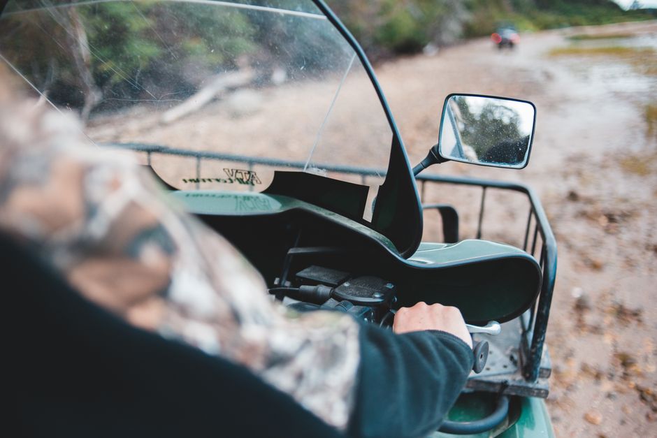 Close-up of a person driving a quad bike on an off-road, muddy trail.