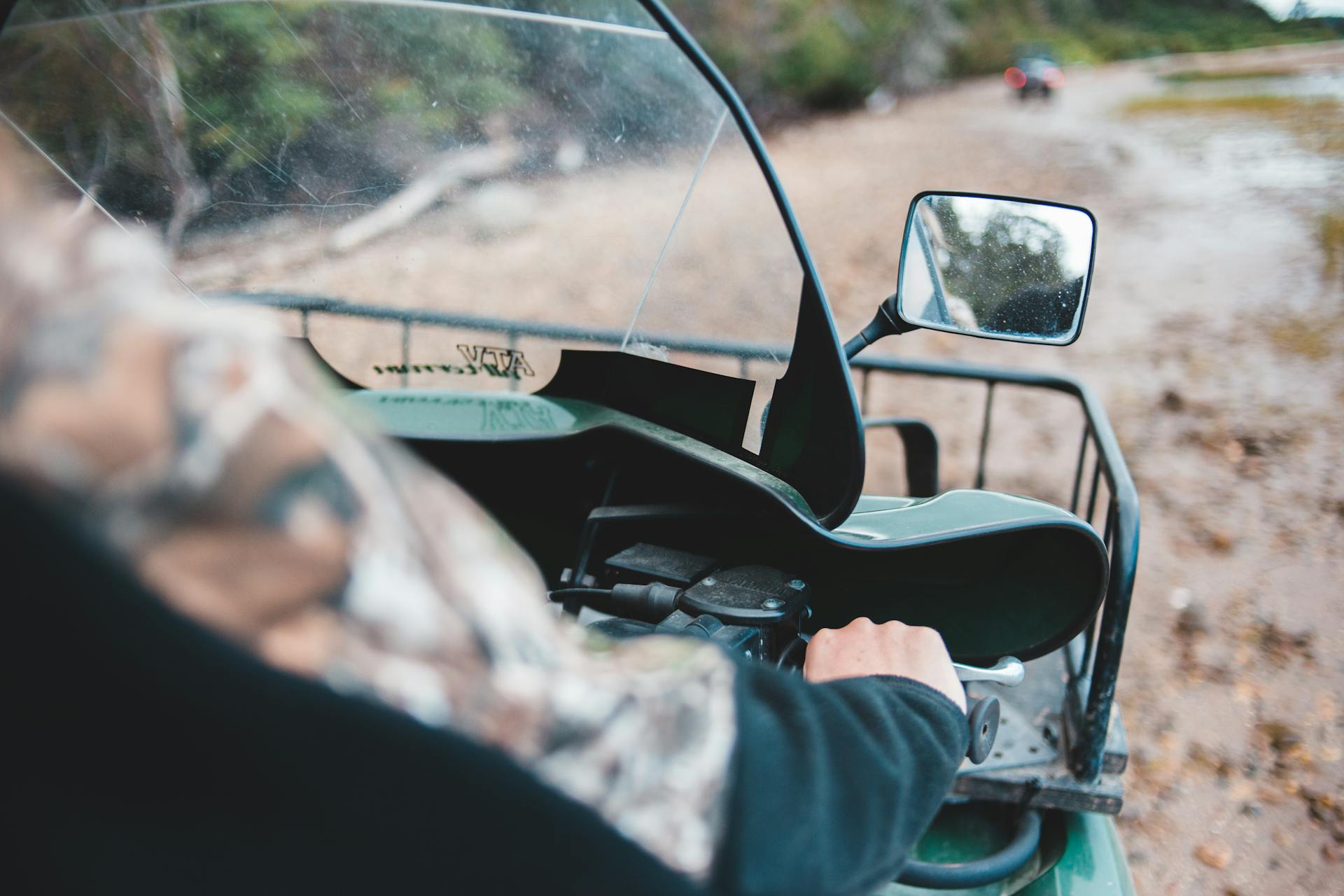 Close-up of a person driving a quad bike on an off-road, muddy trail.