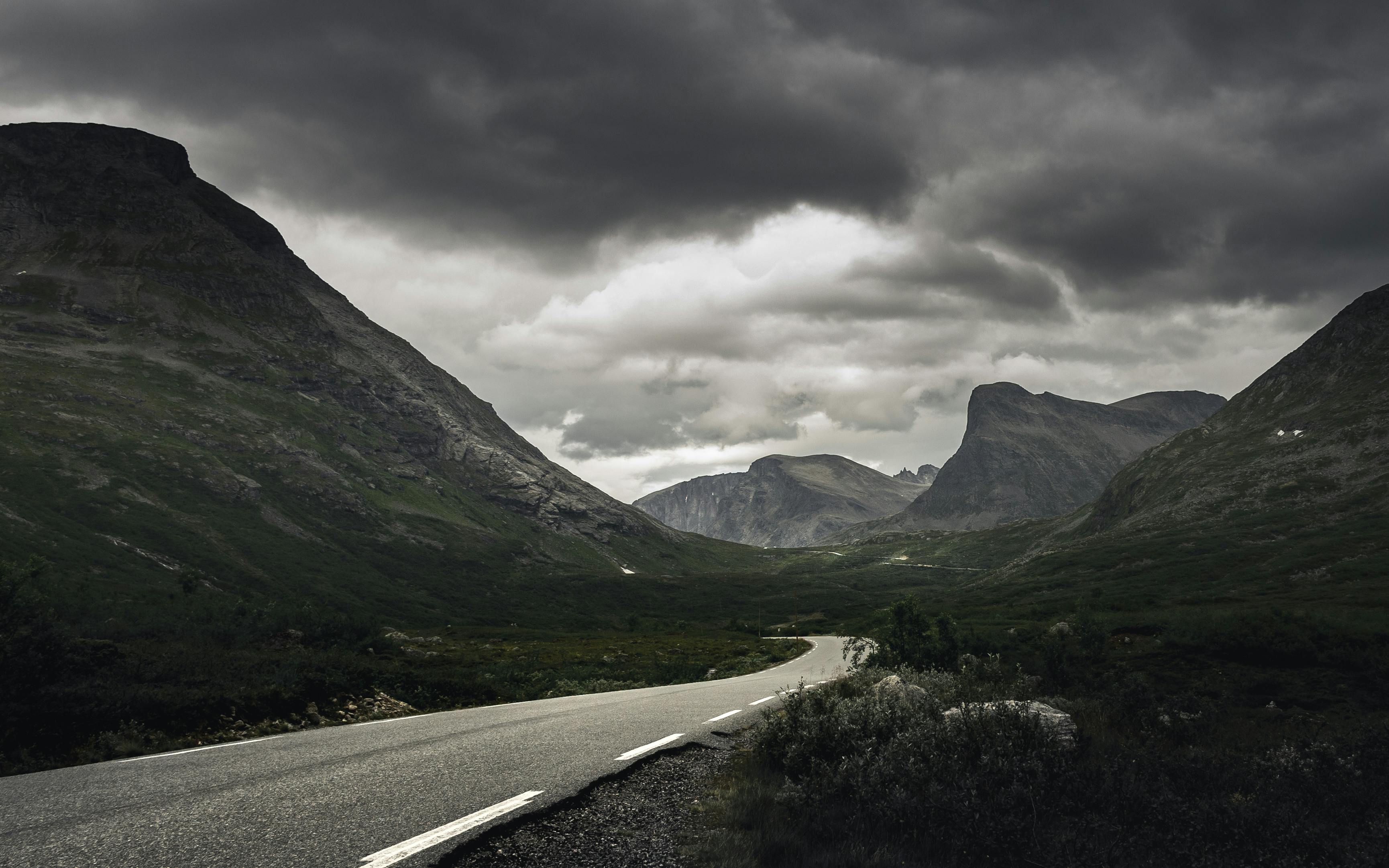 gray asphalt road between green mountains under gray cloudy sky