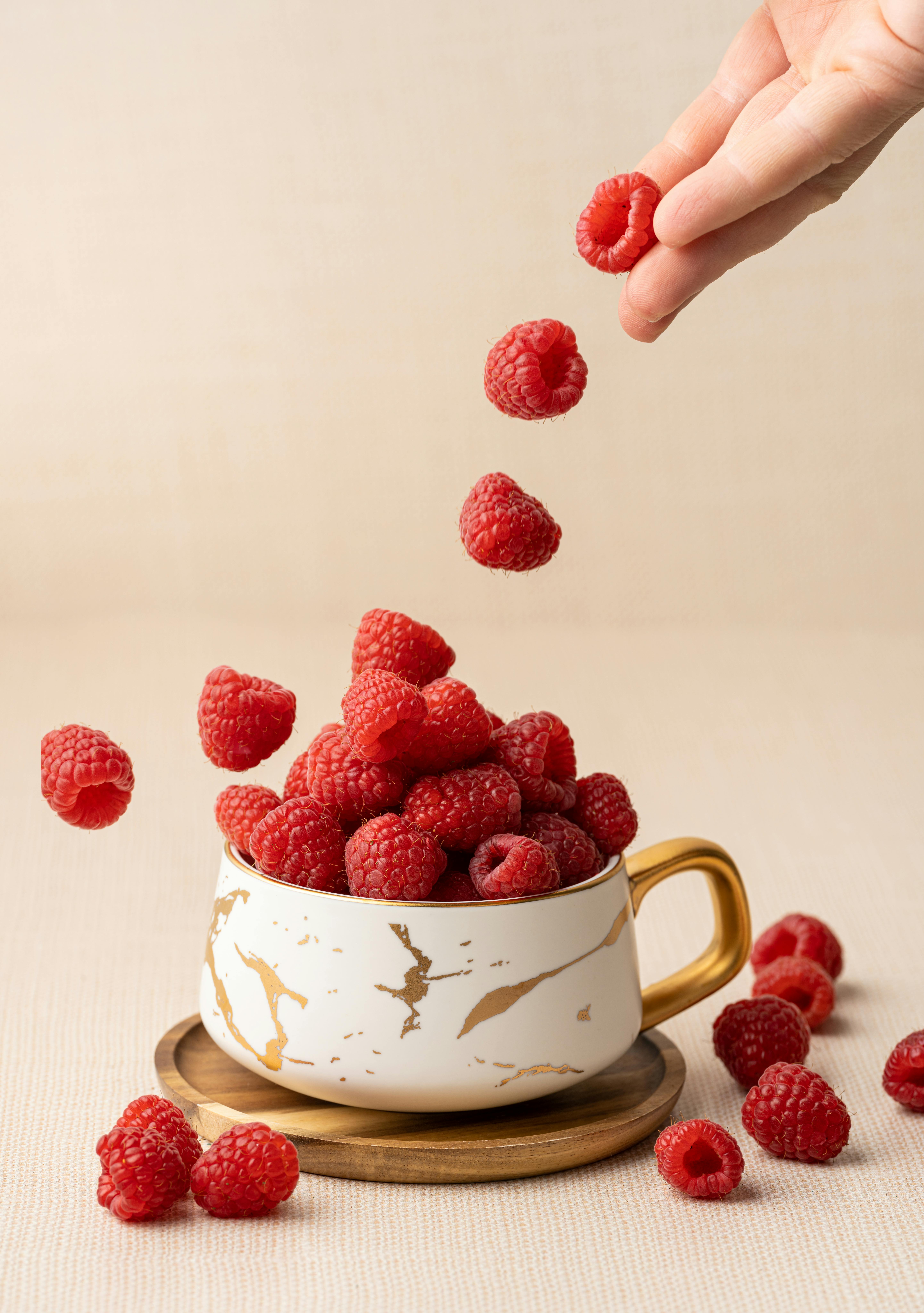 Close-up of raspberries cascading into an elegant cup on a beige background.