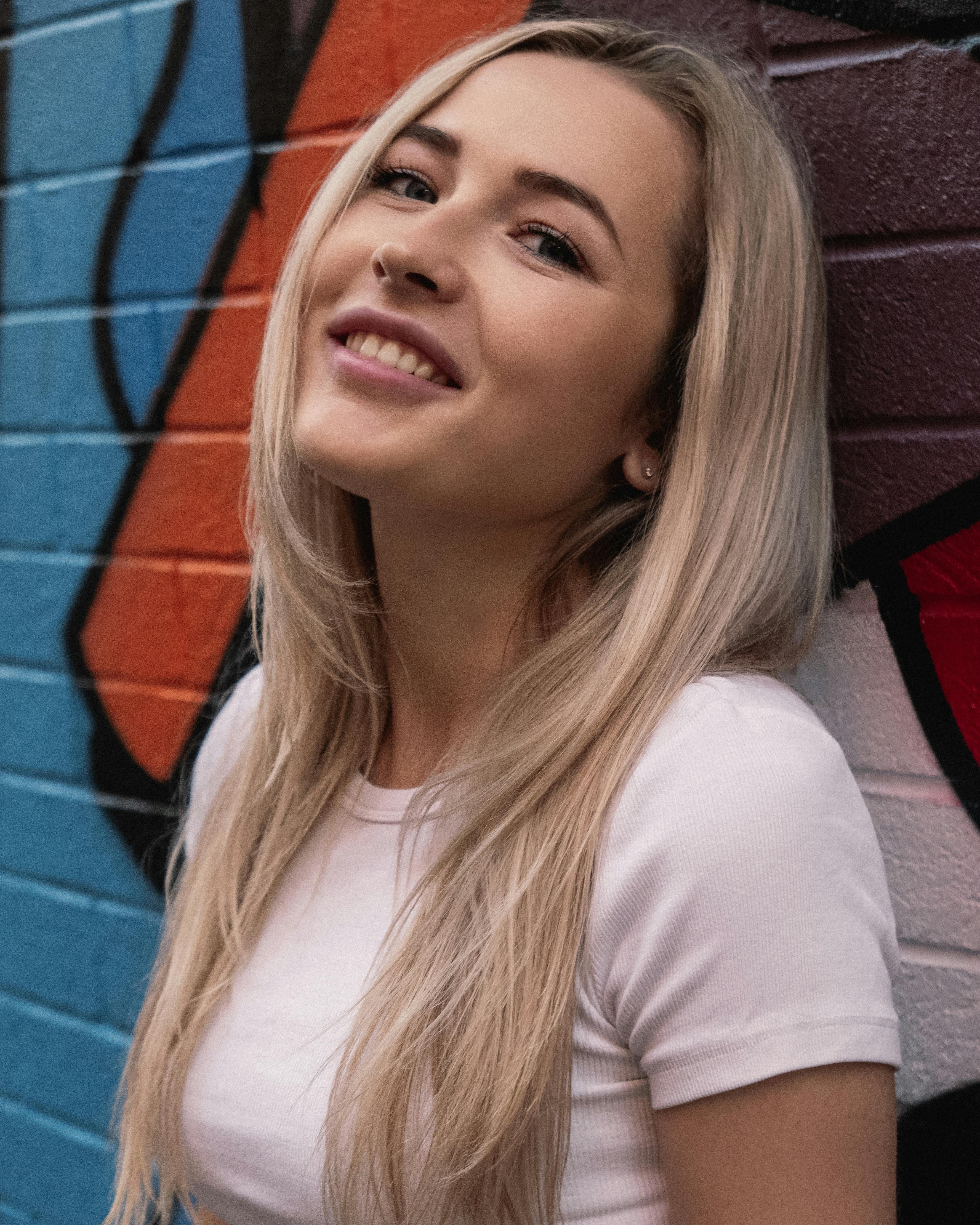 Portrait of a smiling woman standing in front of colorful graffiti, showcasing urban art vibes.