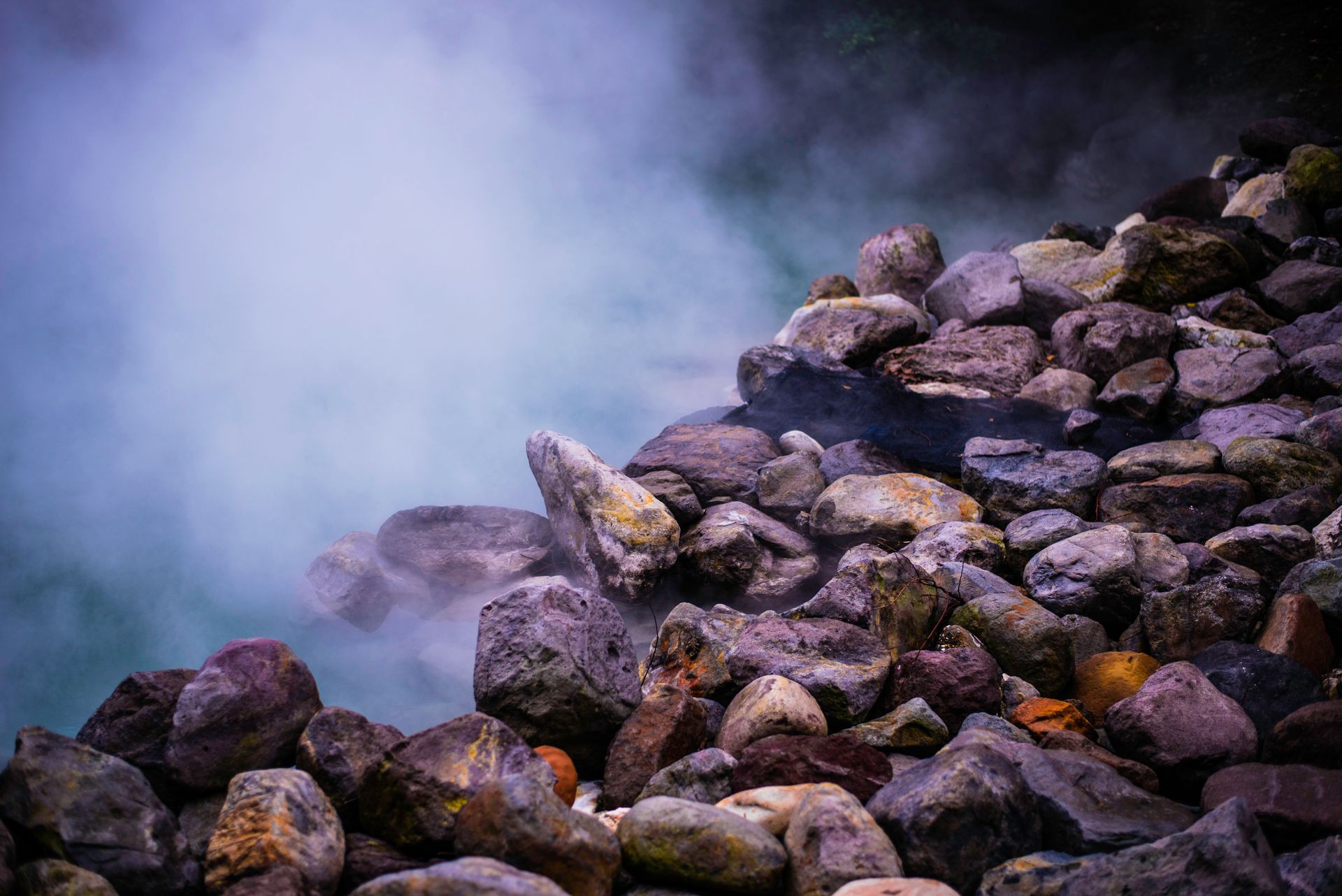 A scenic view of steaming geothermal hot springs surrounded by colorful boulders, creating a tranquil natural scene.
